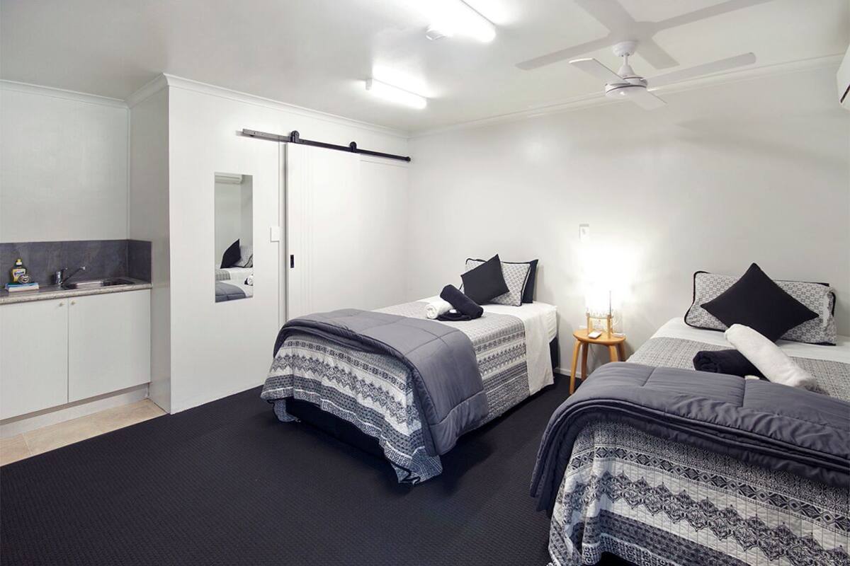 A bedroom with two beds, a small bedside table, a nightstand, a wardrobe, and a mirror.