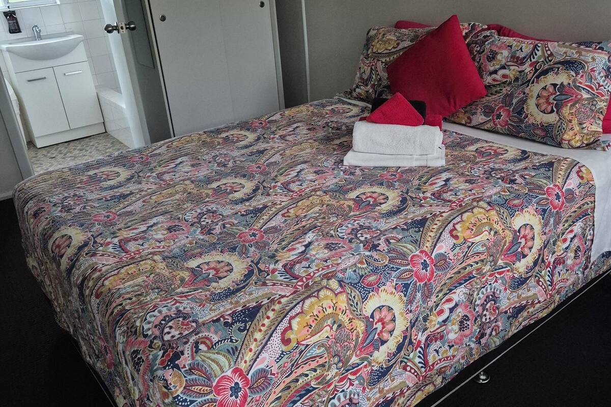 A bedroom with a large bed, a bedside table, a wardrobe, a bathroom with a sink and mirror, and a door.