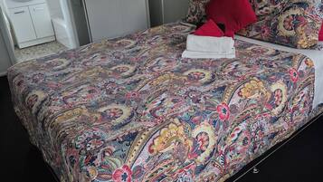 Quarto com cama grande, mesa de cabeceira, guarda-roupa, banheiro com pia e espelho, e uma porta.