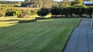A well-maintained lawn with a paved walkway and a view of trees and hills in the distance.