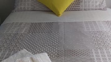 A bed with patterned bedding, a yellow pillow, and a folded towel with a striped towel on it.
