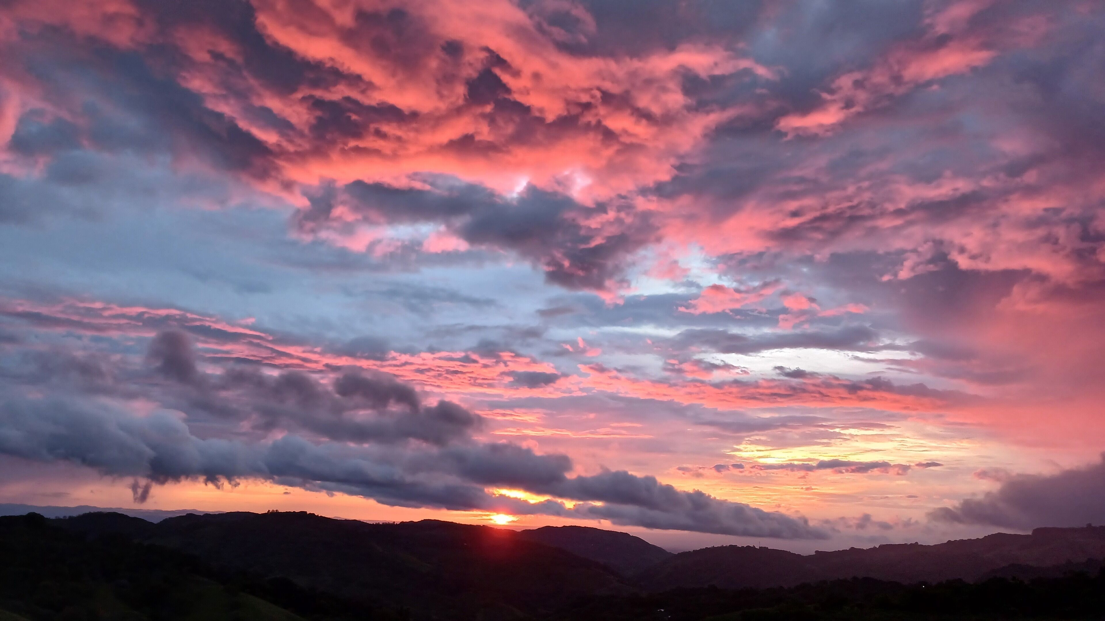 Een zonsondergang boven een bergachtig landschap met wolken.