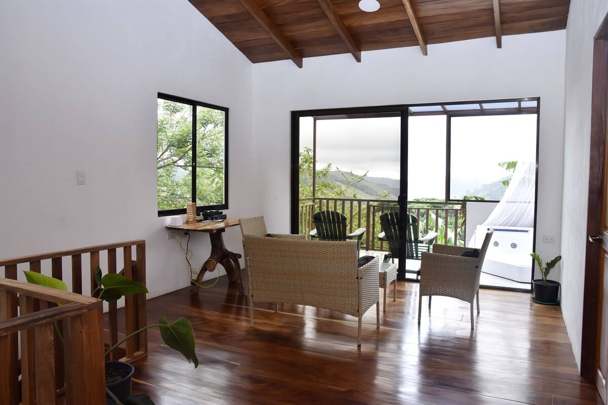 A spacious room with a wooden ceiling, large sliding glass doors leading to a balcony, wicker furniture, and a wooden floor.