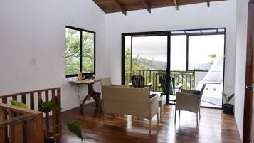 Una habitación amplia con techo de madera, grandes puertas correderas de vidrio que dan a un balcón, mobiliario de mimbre y suelo de madera.