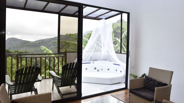 Un balcón con mobiliario de mimbre, bañera de hidromasaje y vista a exuberante vegetación.