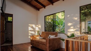 Una habitación amplia con suelo de madera, un sofá marrón, un ventanal con vistas a zonas verdes y una barandilla de madera.