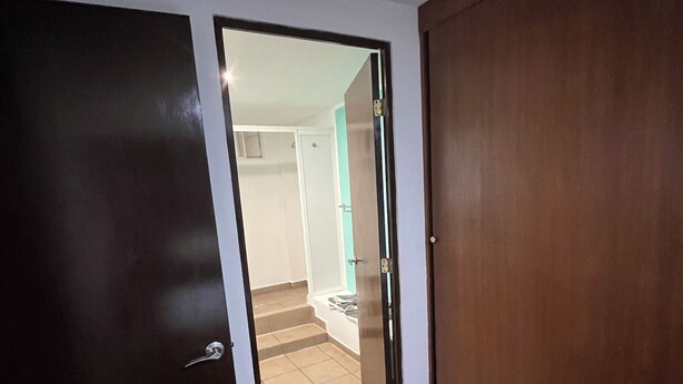 Una habitación con la puerta cerrada, un armario de madera y un suelo de baldosas que conduce a una escalera.