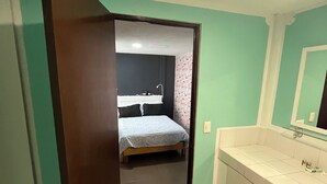 Una habitación con cama, un baño con lavamanos y una puerta que da a otra habitación.