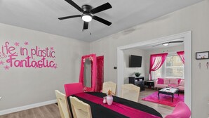 A dining area with a black tablecloth, pink chairs, and a ceiling fan.