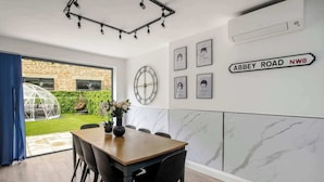 A dining area with a wooden table and chairs, a wall clock, framed artwork, and a sign indicating 'Abbey Road NW8'. - Stunning 4BR 3BA in the ♥️ of London ❄️ Air Con. 🌿 Private Garden | Sleeps 10 (Greater London)