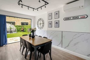 A dining area with a wooden table and chairs, a wall clock, framed artwork, and a sign indicating 'Abbey Road NW8'.