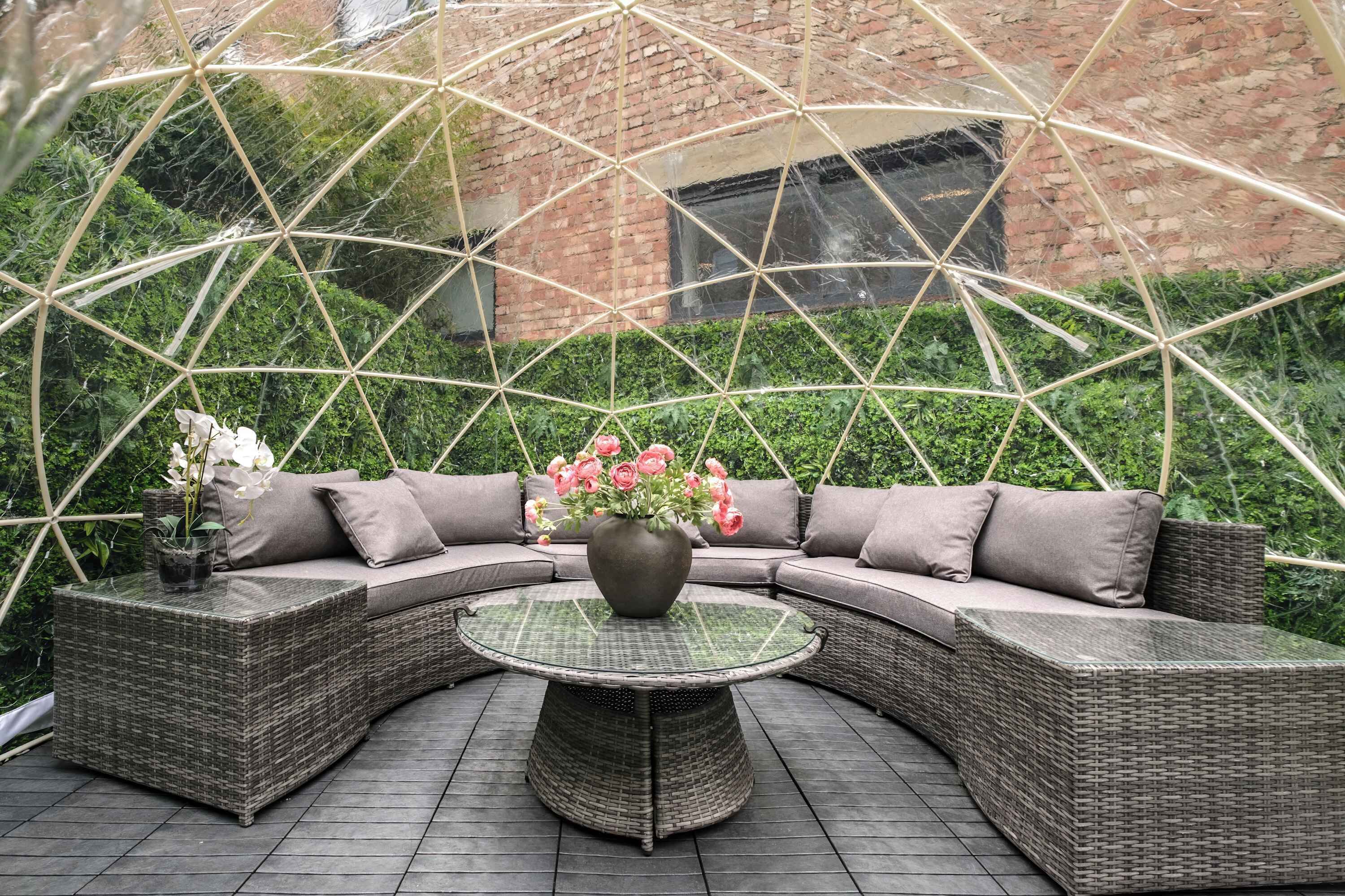 Un espace extérieur abrité, aménagé avec une table ronde, un canapé confortable et un pot de fleurs.
