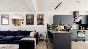 A modern kitchen with dark cabinetry, a central island, and a dining area with a dark blue sofa. - Stunning 4BR 3BA in the ♥️ of London ❄️ Air Con. 🌿 Private Garden | Sleeps 10 (Greater London)
