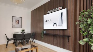 A modern living room with a mounted TV displaying a PS5, a dining area with a table and chairs, and a potted plant. - Elegant 2BR in the ♥️ of Marylebone ❄️ Air Conditioning ☀️ Terrace (Greater London)