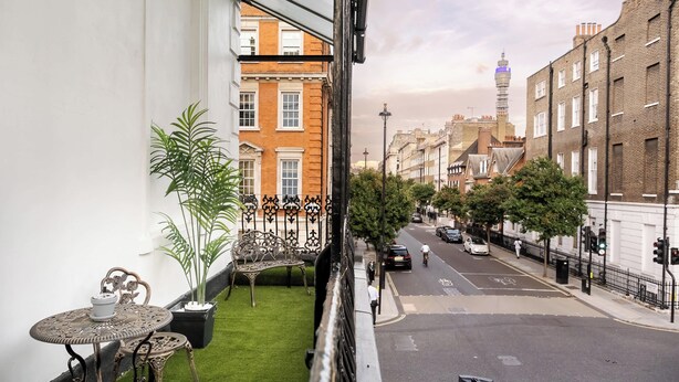 A balcony with a small table and chairs, a potted plant, and a view of a street with buildings and a tower. - Elegant 2BR in the ♥️ of Marylebone ❄️ Air Conditioning ☀️ Terrace (Greater London)