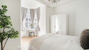 A bedroom with a large bed, a wardrobe, a potted plant, and a window with curtains. - Elegant 2BR in the ♥️ of Marylebone ❄️ Air Conditioning ☀️ Terrace (Greater London)
