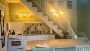 A kitchen with a central island, white cabinetry, a stove, and a sink. There is a staircase leading to another level. - Charming loft cottage in tranquil Germantown with WiFi, AC (Germantown)