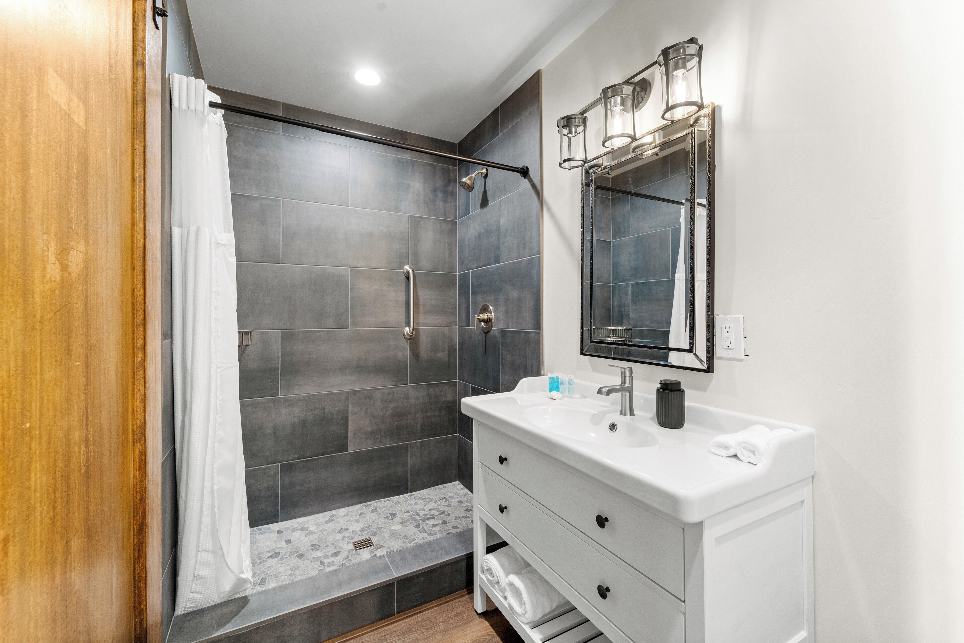 A modern bathroom with a shower, white vanity, and a mirror with lights.