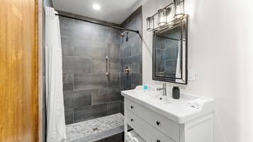 A modern bathroom with a shower, white vanity, and a mirror with lights.