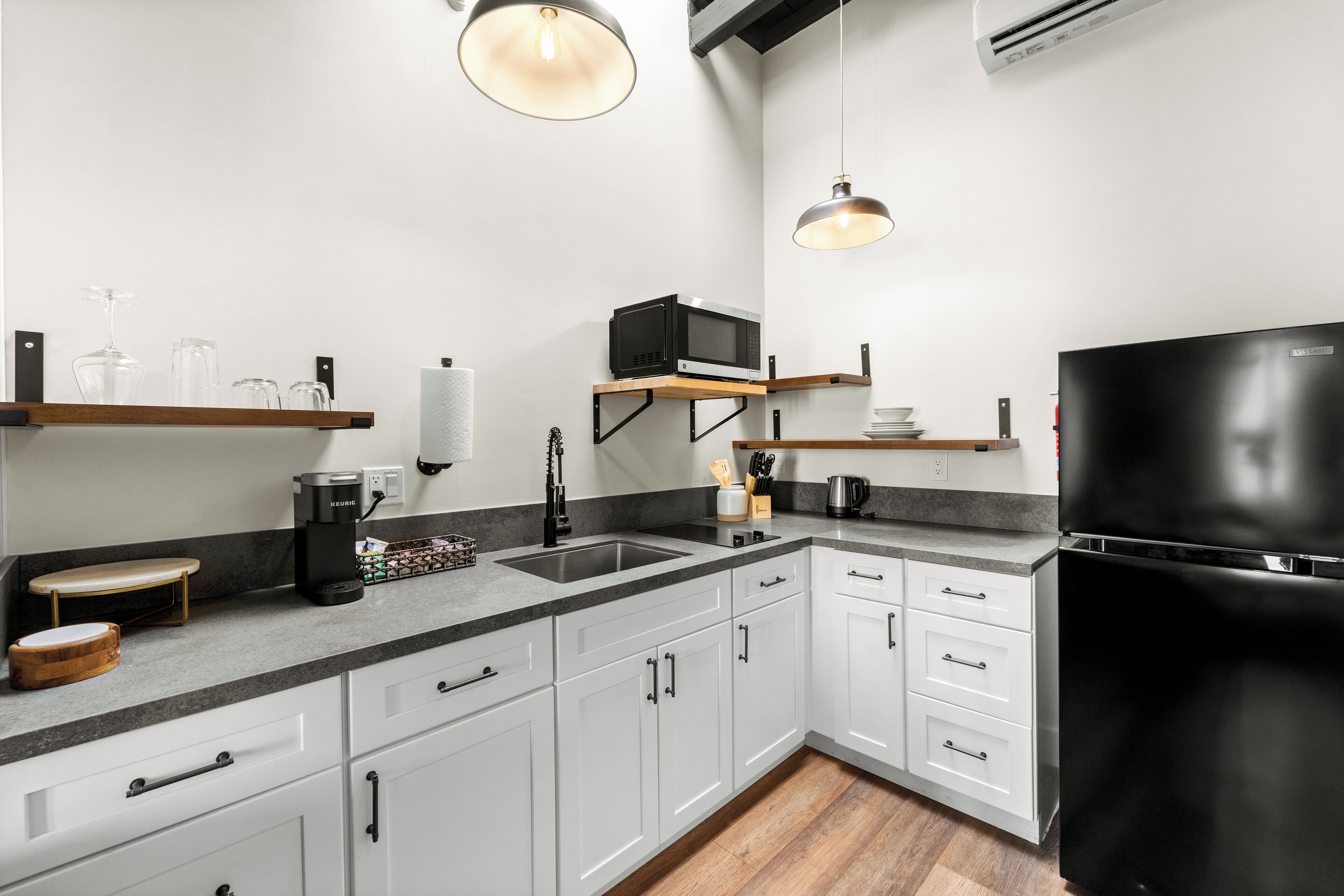 A modern kitchen with white cabinets, a black refrigerator, and a coffee maker.
