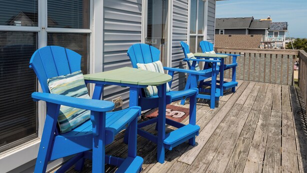 A wooden deck with blue Adirondack chairs and a small table, overlooking a beach. - Charming 4-bedroom house.  Walking distance to the Beach and Restaurants! (Kill Devil Hills)