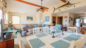 A spacious living room with a large dining table, white chairs, and a ceiling fan. - Charming 4-bedroom house.  Walking distance to the Beach and Restaurants! (Kill Devil Hills)