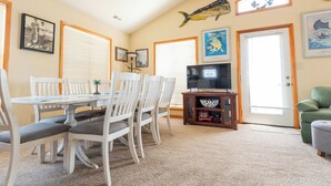 A dining area with a white table and chairs, a television on a wooden stand, and framed fish pictures on the walls. - Charming 4-bedroom house.  Walking distance to the Beach and Restaurants! (Kill Devil Hills)