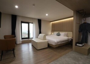 A modern hotel room with a bed, a seating area, and a wardrobe.