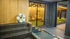 A modern interior with a wooden wall, a poolside area with a lounge chair, and a view of an outdoor garden. - H AVENUE (Busan)