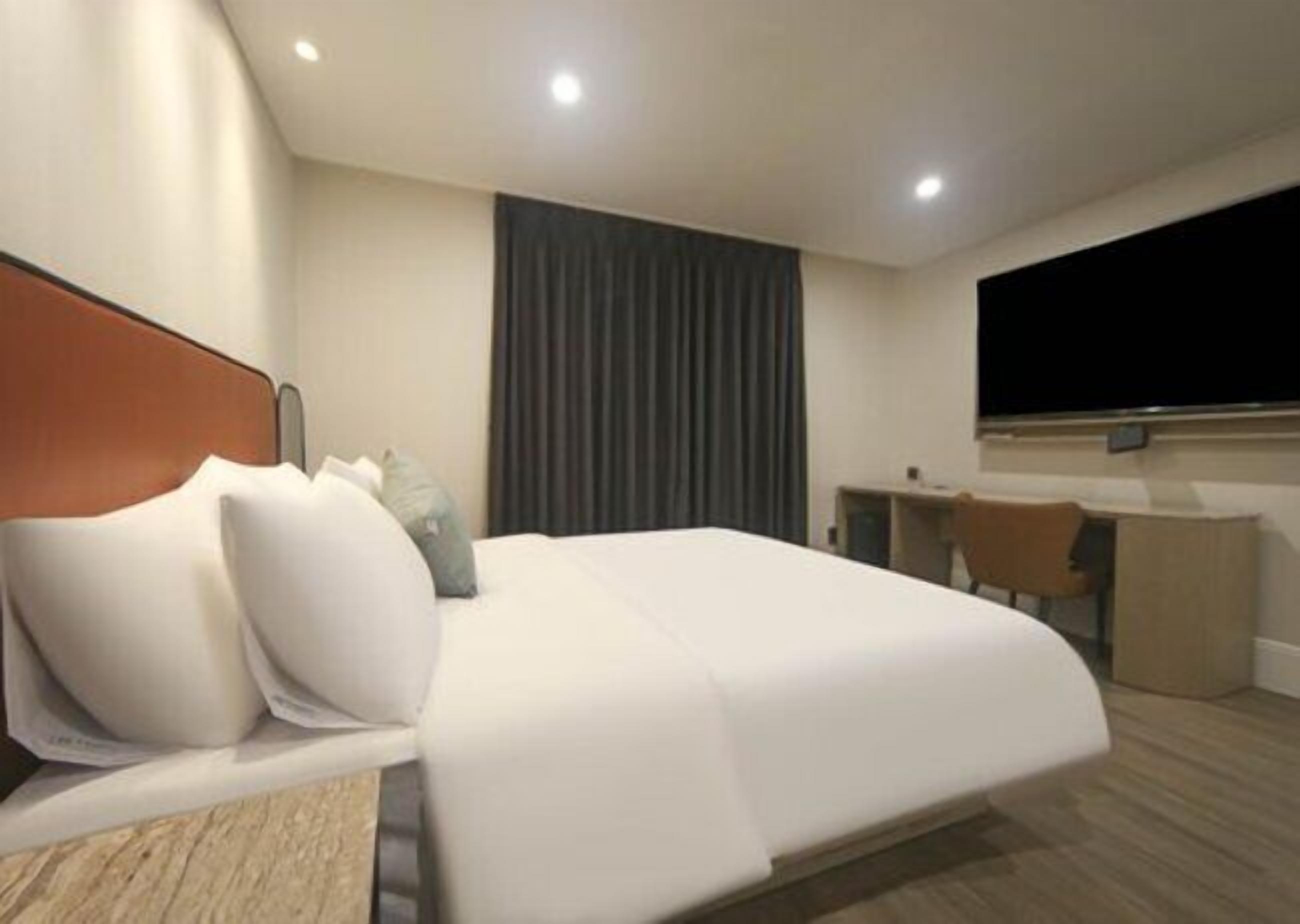 A modern hotel room with a large bed, a desk, and a television.