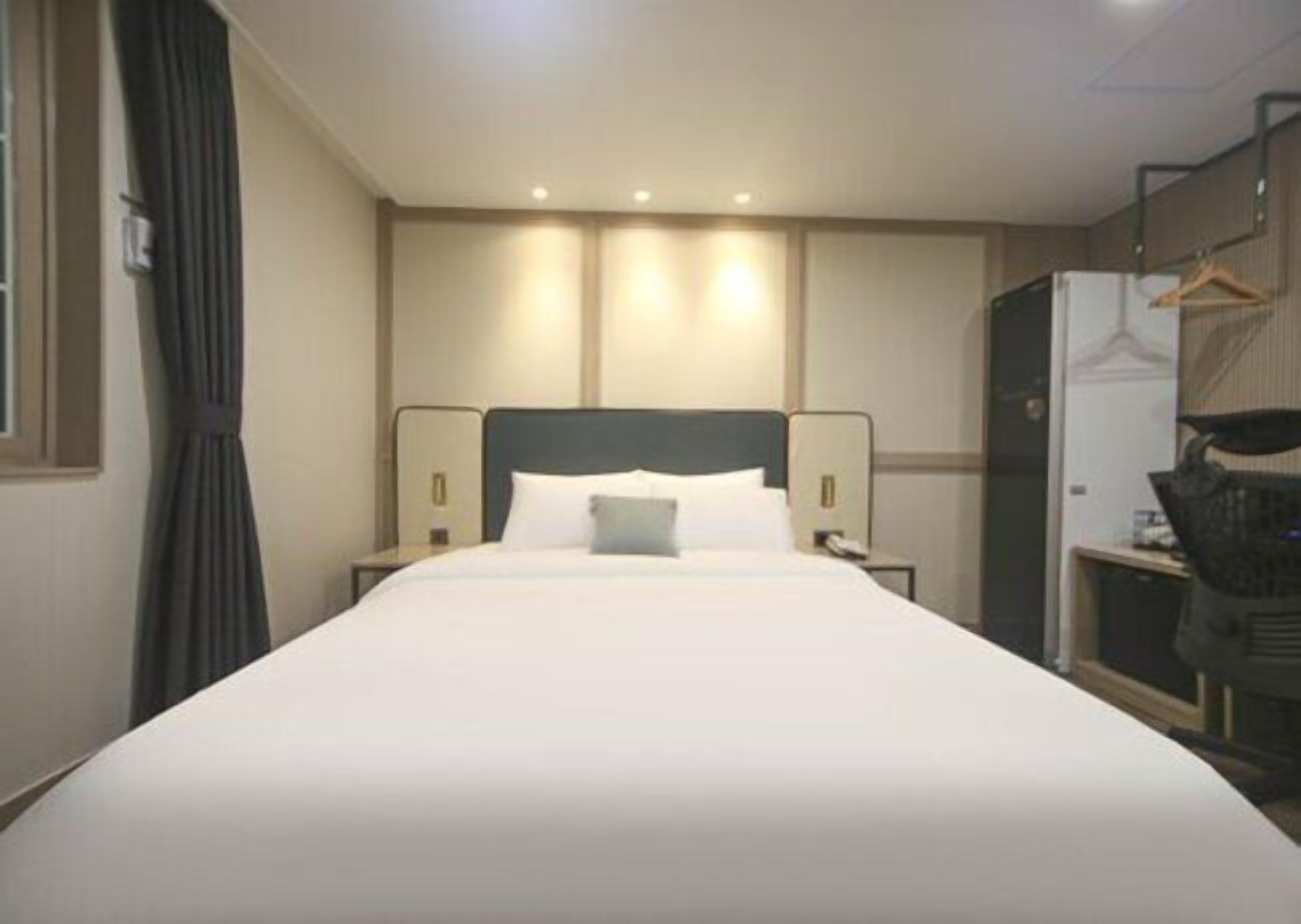 A hotel room with a large bed, bedside tables, a wardrobe, and a desk with a chair.