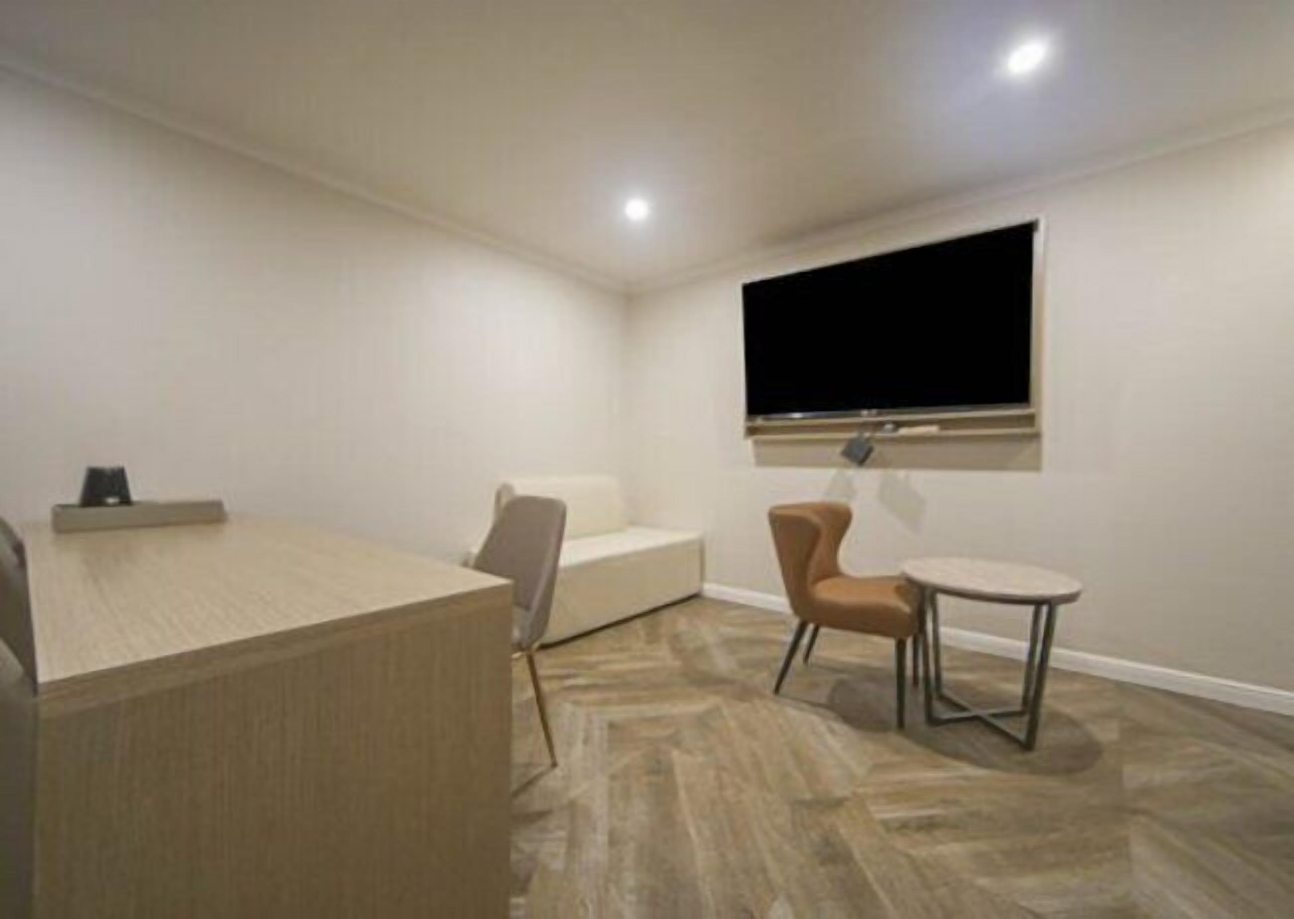 A small, modern room with a sofa, a coffee table, and a TV mounted on the wall.