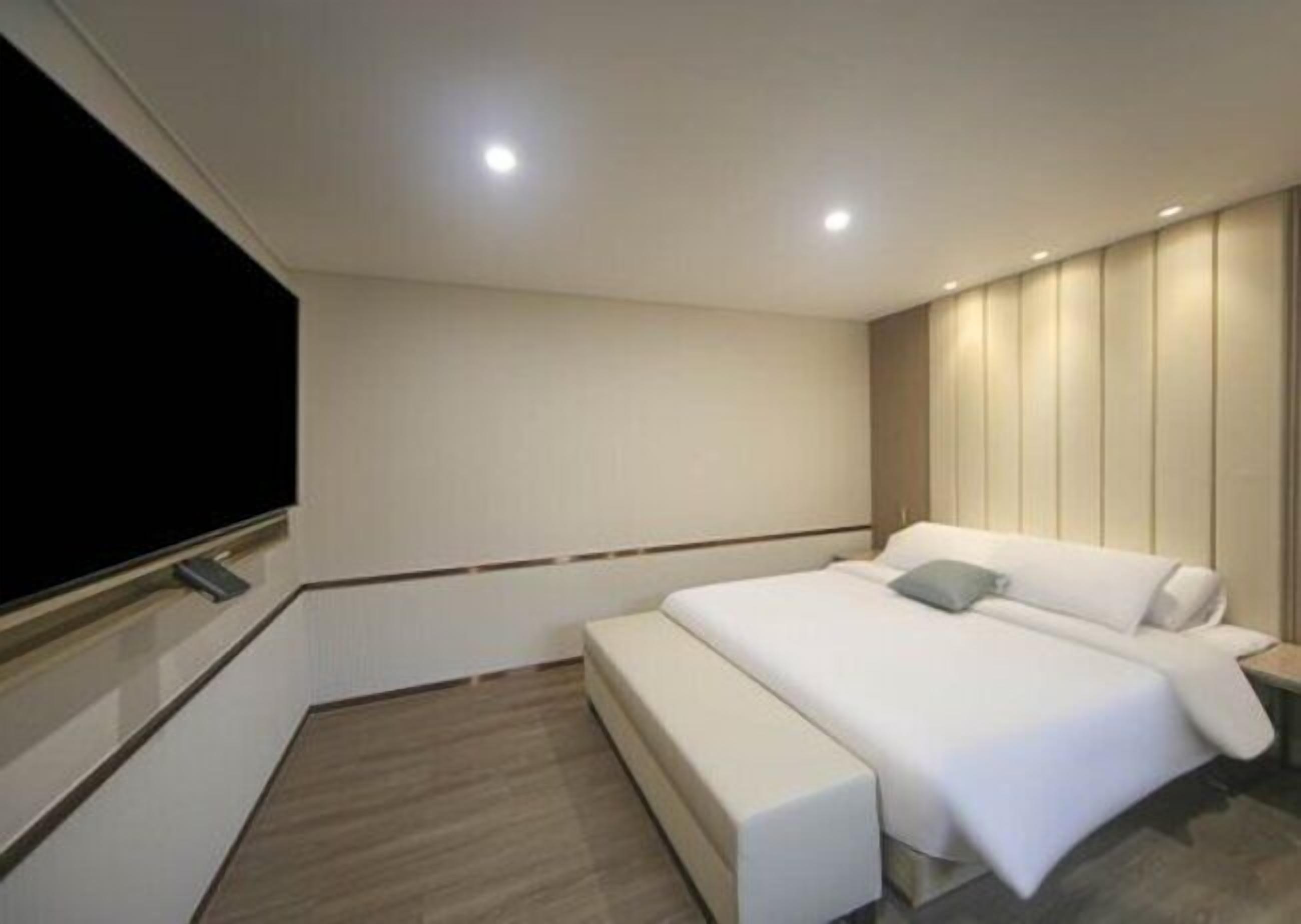 A modern hotel room with a large bed, a bench, a flat-screen TV, and a wooden panel wall.