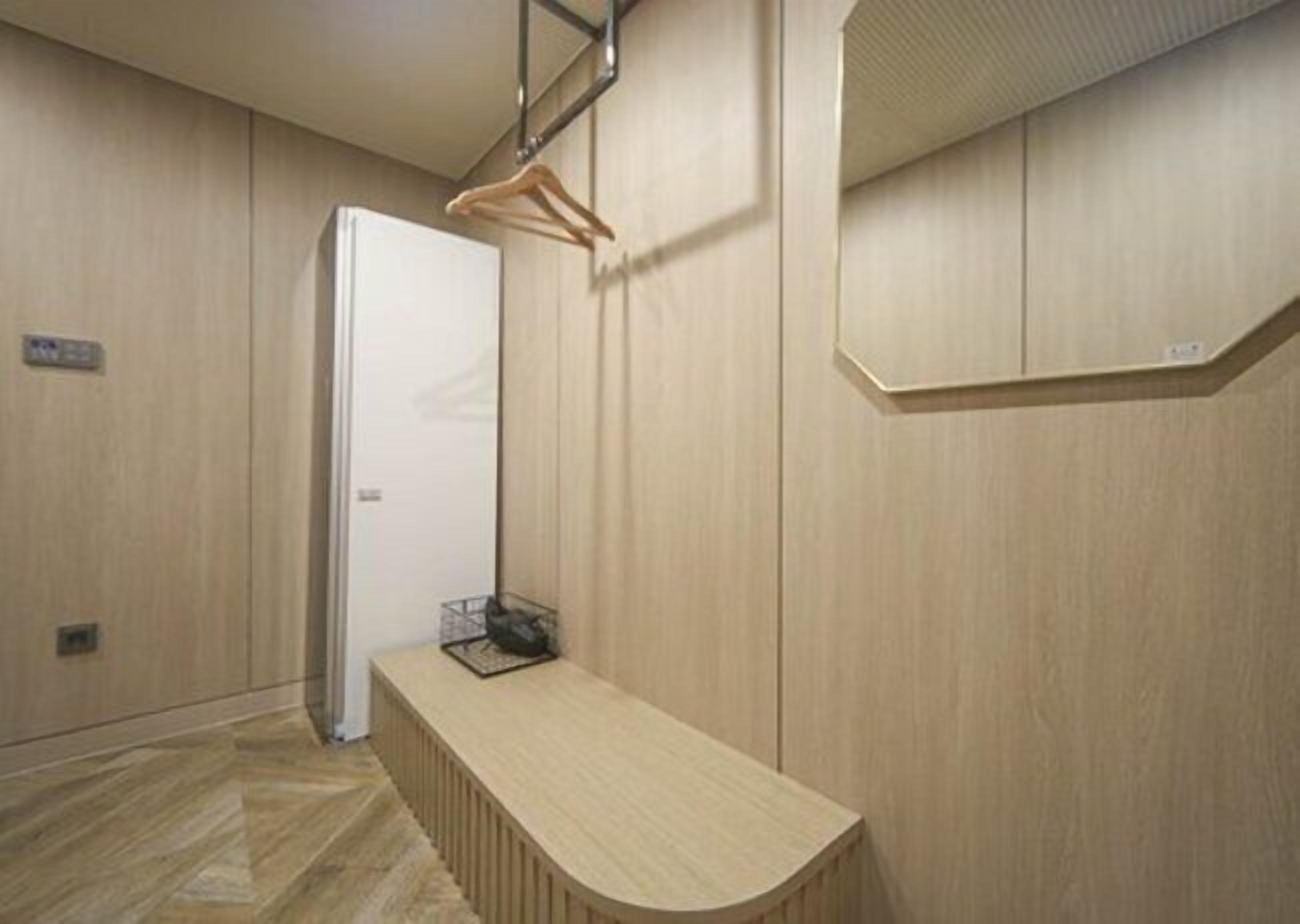 Una camera d'albergo con pavimento in legno, una panca di legno, una porta bianca e uno specchio appeso al muro.