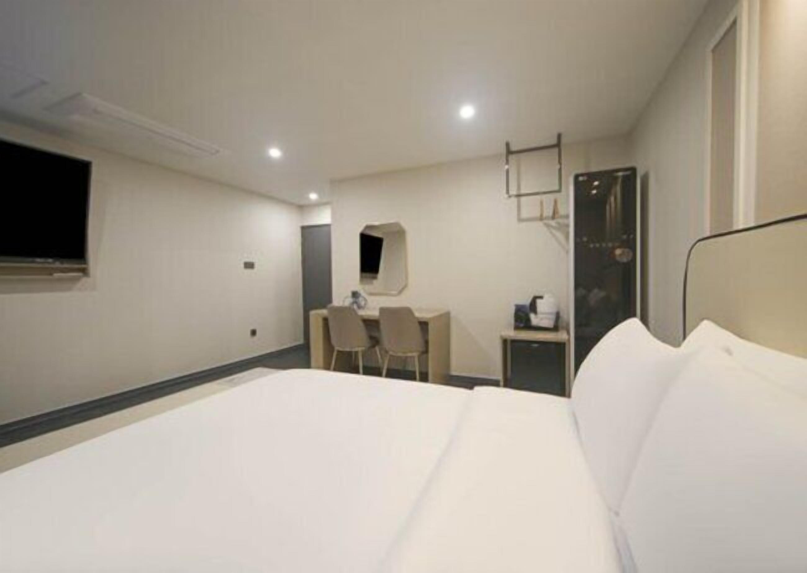 Una habitación de hotel con una cama grande, un escritorio con dos sillas, un televisor en la pared y una mesita de noche con lámpara.