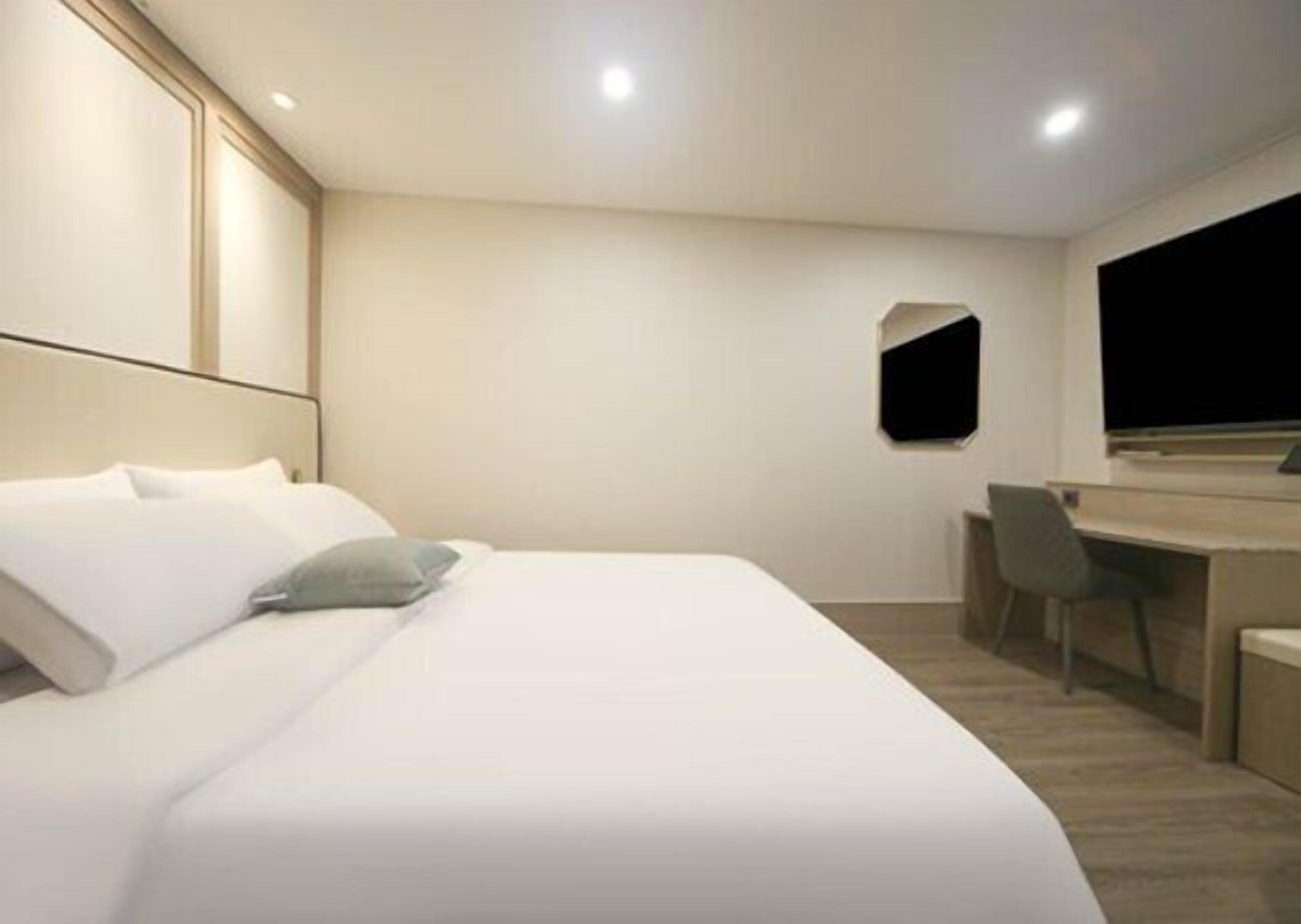 A modern hotel room with a large bed, a desk, and a flat-screen TV.