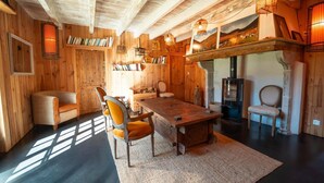 A rustic wooden room with a large wooden table, two chairs, a bookshelf, and a fireplace.