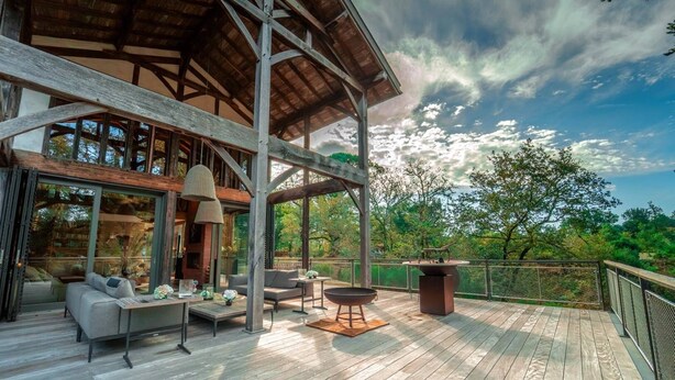 A wooden deck with outdoor furniture, a fire pit, and a view of the surrounding forest.