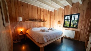 A wooden-paneled room with a bed, bedside lamp, and a window with a view of greenery.