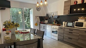 Eine moderne Küche mit Essbereich, mit einem Glastisch, weißen Geräten und Blick auf Grünfläche.