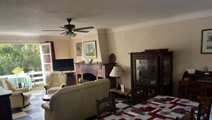 Ein gemütliches Wohnzimmer mit einer Couch, Sesseln, einem Fernseher, einem Kamin und einem Esstisch mit einer Patchworkdecke.