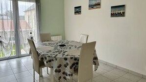 Zona pranzo con un tavolo rotondo, sedie bianche e una tovaglia con motivo a foglie. Sono presenti tre opere d'arte incorniciate appese al muro.