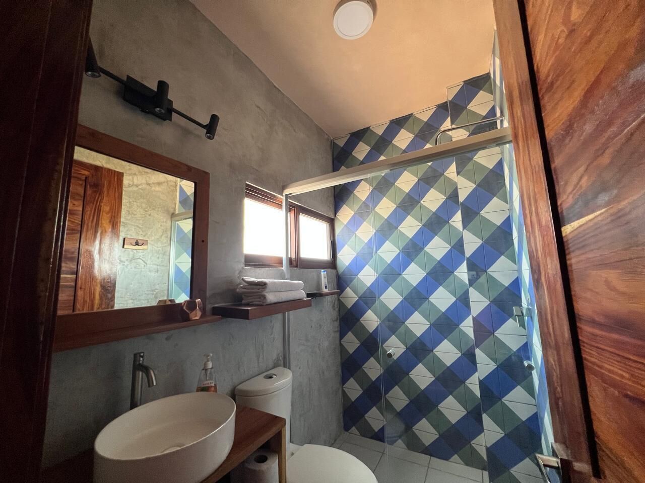 Un baño con tocador de madera, lavabo, inodoro y ducha con un diseño de azulejos geométricos.
