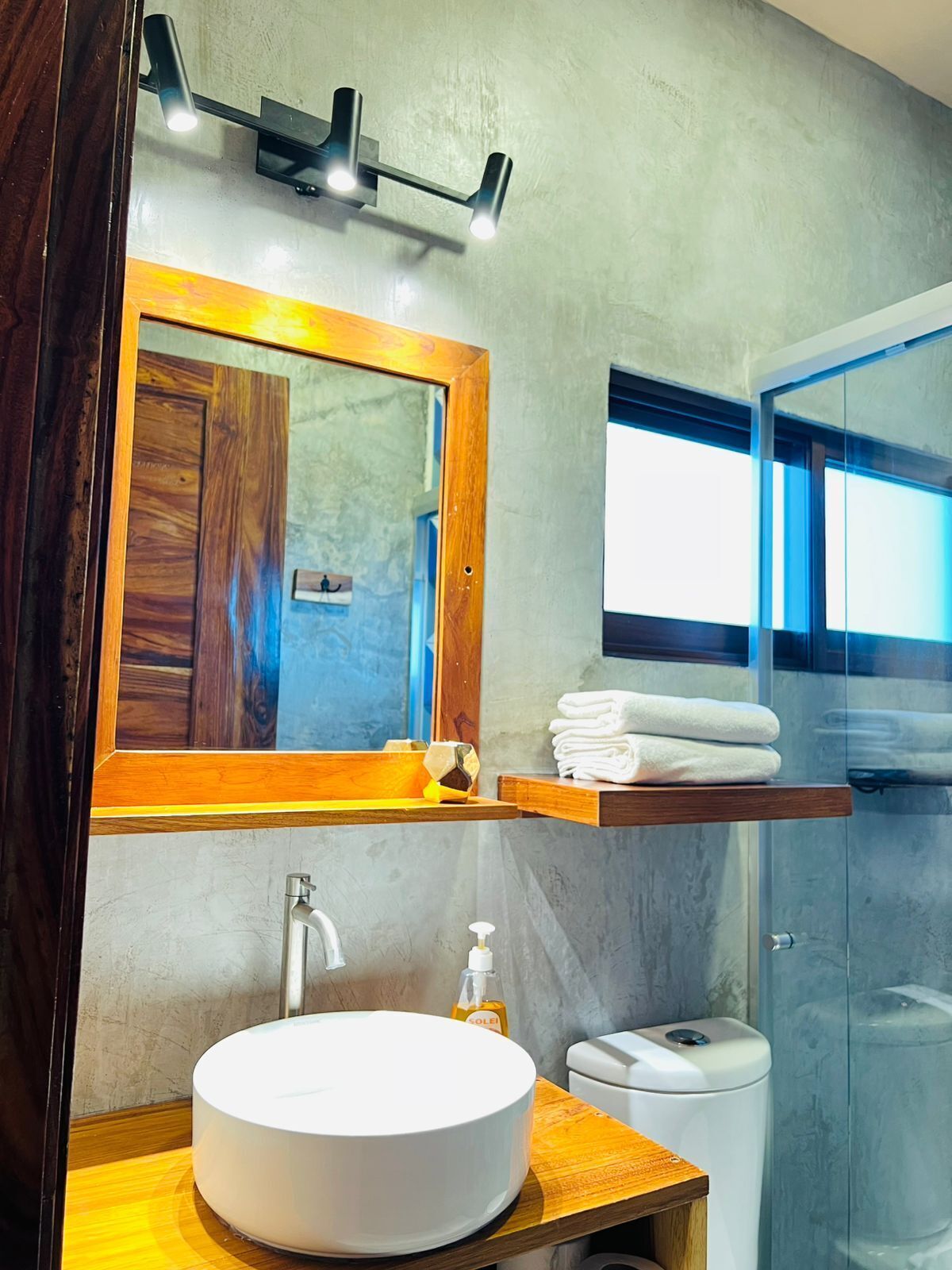 Een moderne badkamer met een grote spiegel, een houten wastafelmeubel, een witte wasbak en een douchecabine van glas.