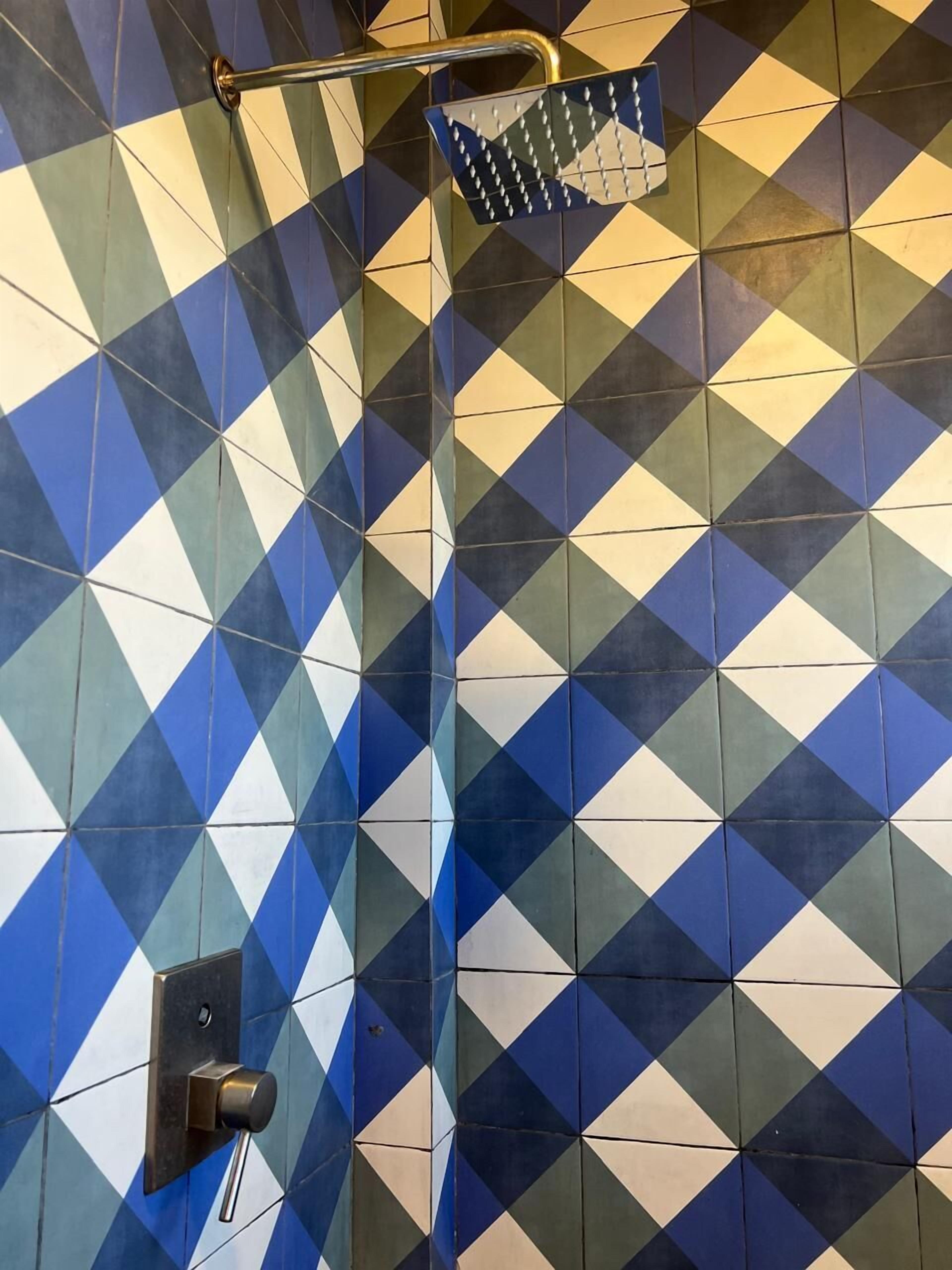 Un baño con pared de azulejos de diseño geométrico, un cabezal de ducha y una manija metálica.