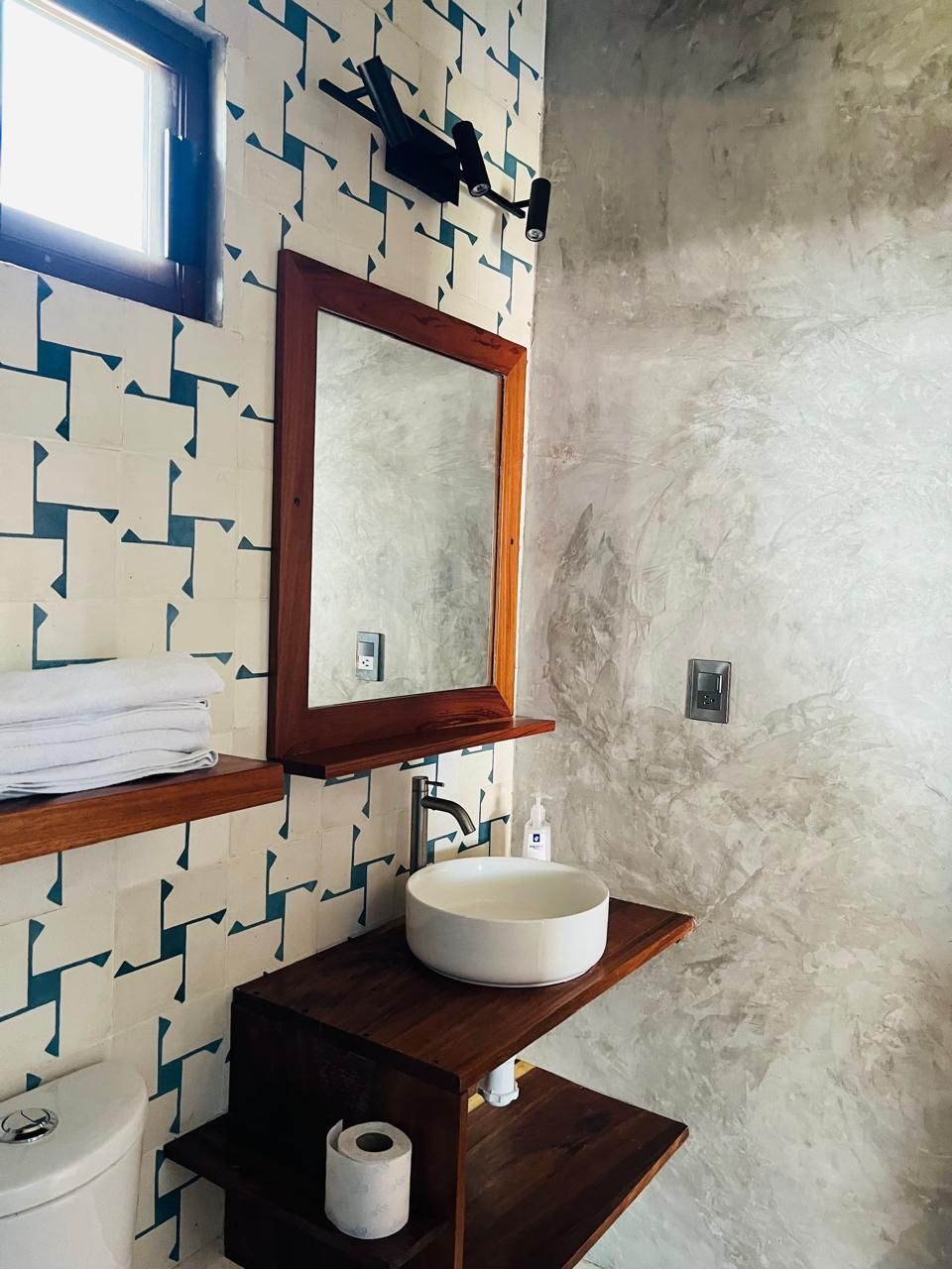 A bathroom with a geometric patterned wall, a wooden vanity, a round sink, a mirror, and a toilet.
