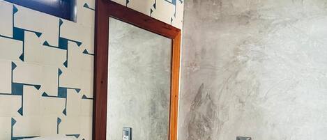 A bathroom with a geometric patterned wall, a wooden vanity, a round sink, a mirror, and a toilet.