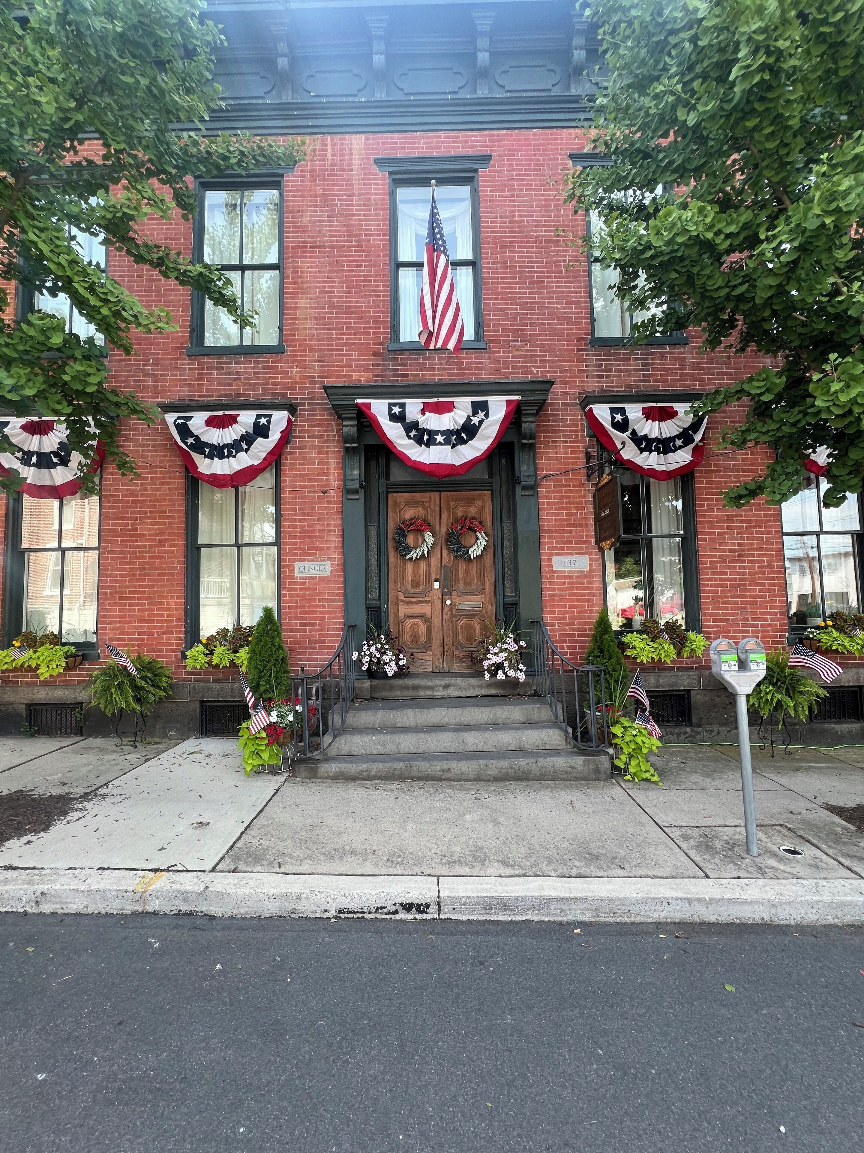 A brick building with a wooden front door, American flags, and patriotic decorations.