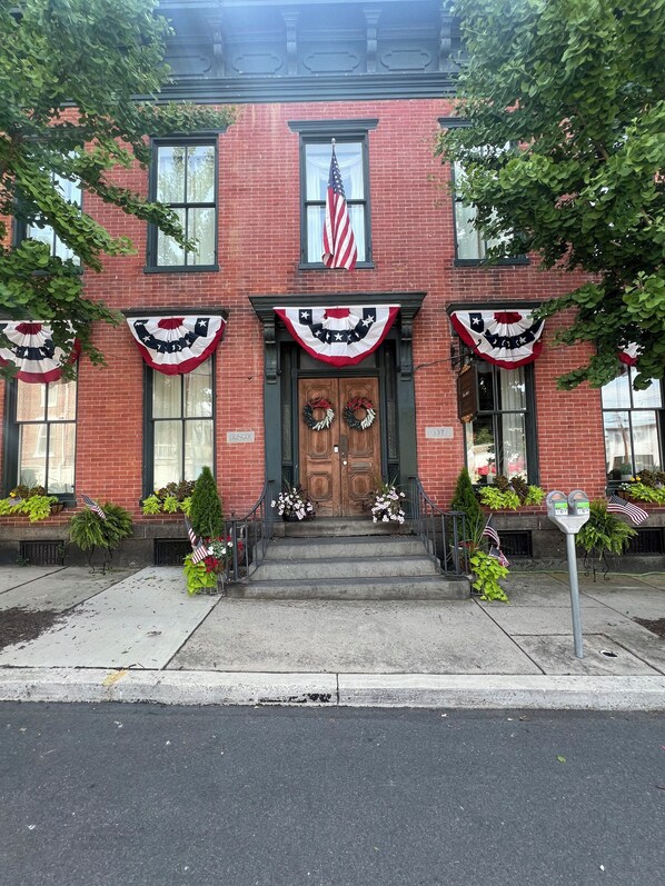 Un bâtiment en briques avec une porte d’entrée en bois, des drapeaux américains et des décorations patriotiques.