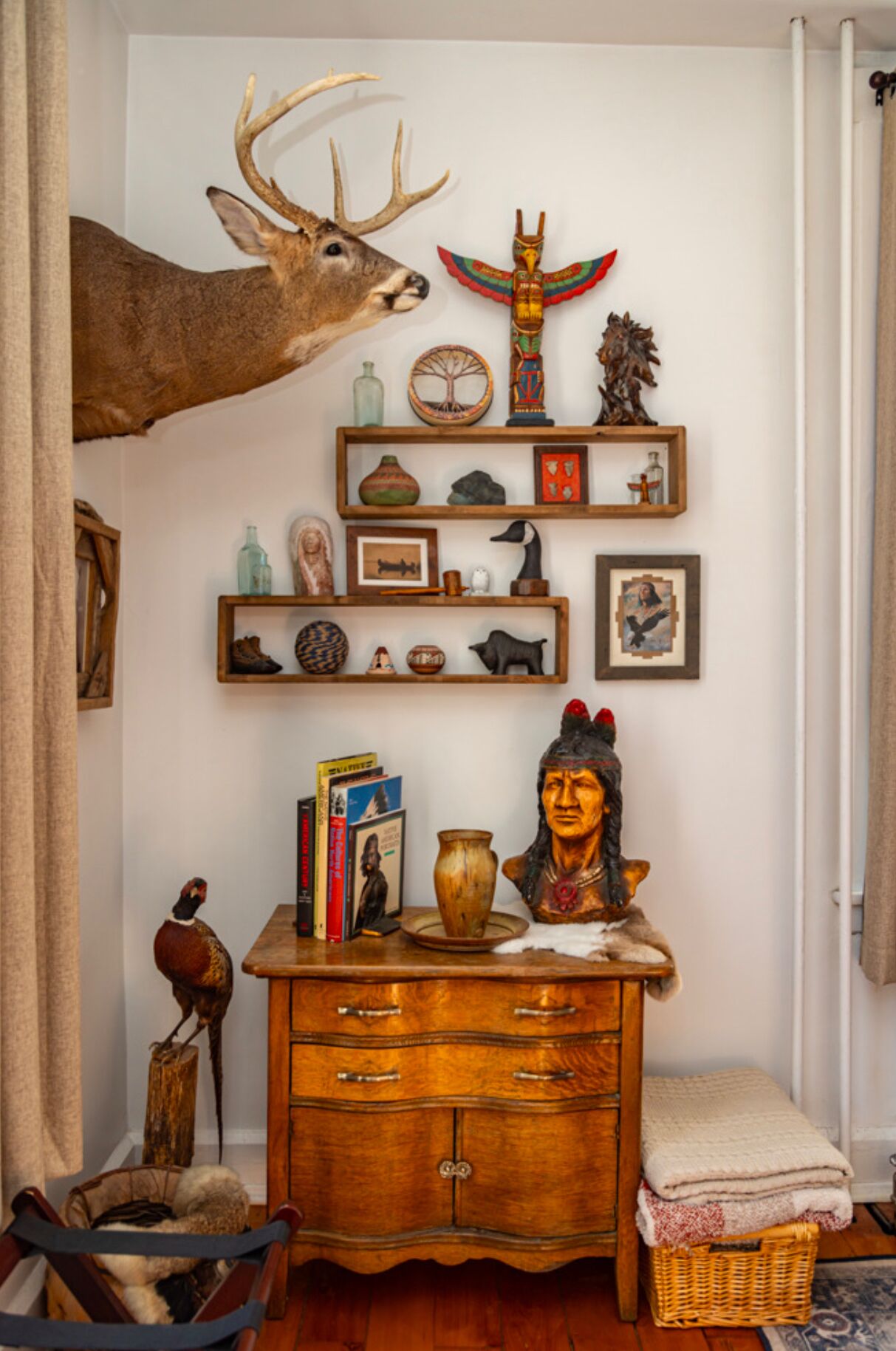Een kamer met een hertenkop aan de wand, een houten kast met diverse voorwerpen, en een plank met decoratieve objecten.